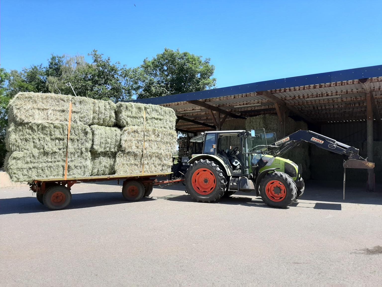 Traktor mit Heuwagen vor Lagerhalle